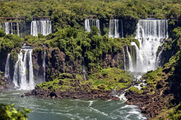 Various waterfalls flow over rocky cliffs, embedded in a lush green landscape, The Iguazu Falls