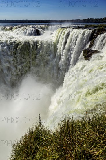A powerful waterfall cascades over steep cliffs, surrounded by lush greenery, The Iguazu Falls