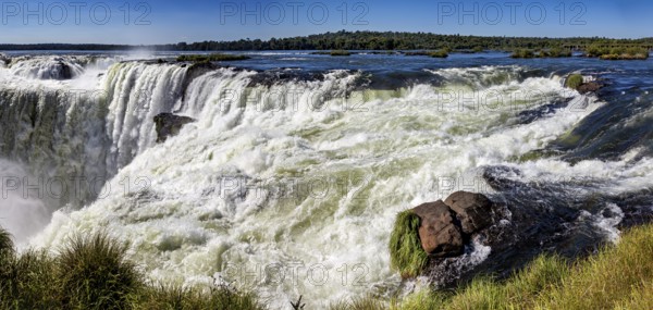 Panoramic view of the raging river and waterfall, surrounded by rocks and lush greenery, The Iguazu