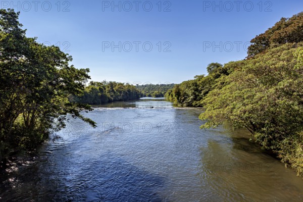 A calm river flows through a forested landscape under a clear blue sky, The Iguazu River between