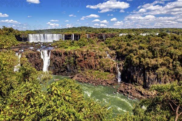 Waterfalls cascade into a river amidst lush vegetation and clear skies, The Iguazu Falls between