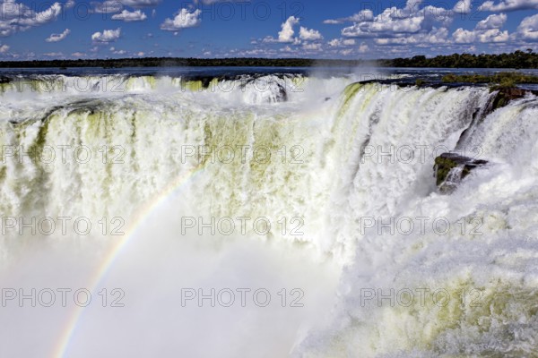 Waterfall with a rainbow over the foaming spray against a cloudy sky, The Iguazu Falls between