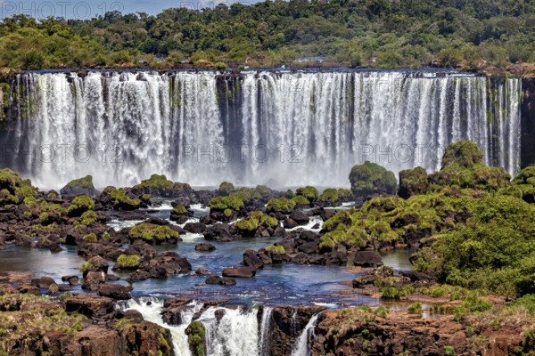 Wide waterfalls cascade over rocks into a river surrounded by lush greenery, The Iguazu Falls