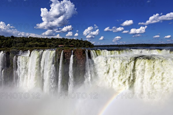 Majestic waterfall with rainbow under a clear sky and scattered clouds, The Iguazu Falls between