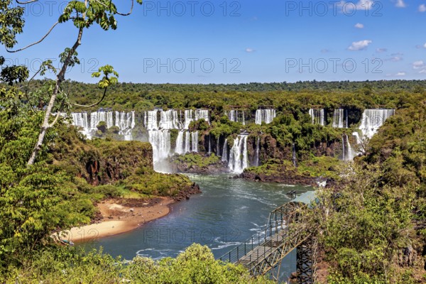 Panoramic view of waterfalls with river, bridge and wooded landscape under a clear sky, The Iguazu