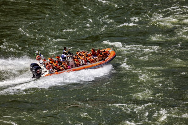 People in an orange-coloured rubber dinghy navigate through turbulent river waters, tourists in a