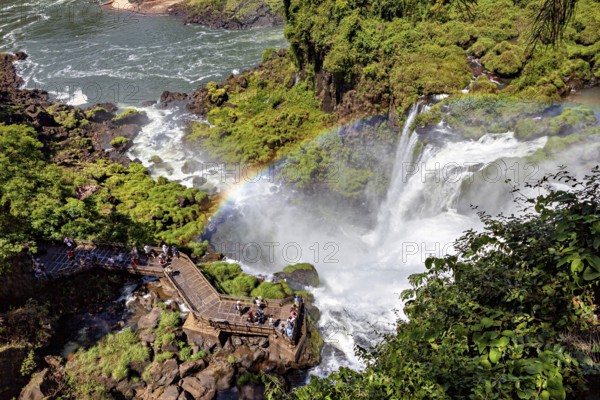 Visitors marvel at the waterfall from a platform above a rainbow on the riverbank, The Iguazu Falls