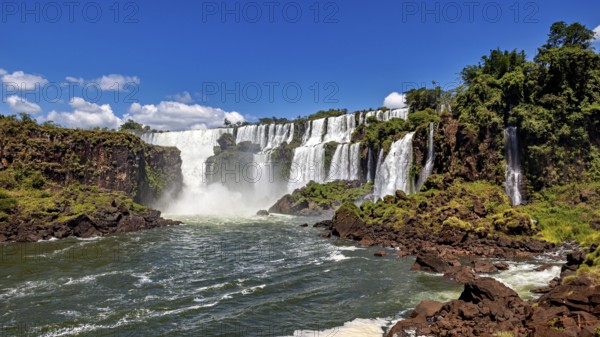 Impressive waterfalls with cascading floods and lush vegetation under a blue sky, The Iguazu Falls