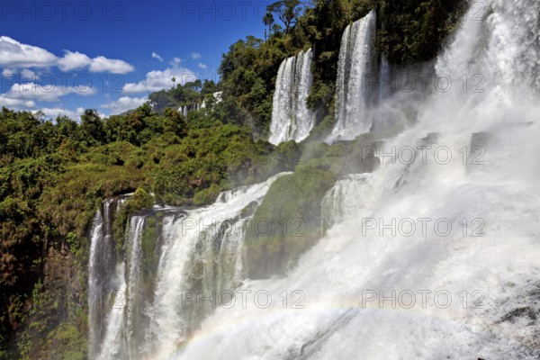 Waterfalls with dense fall and rainbow, embedded in lush forest under a blue sky, The waterfalls of