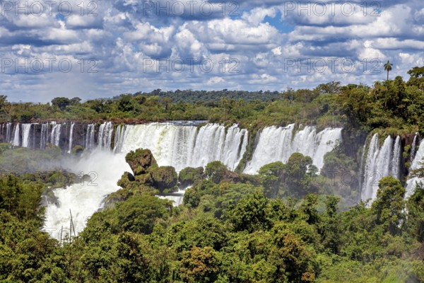 Expansive view of a large waterfall amidst lush green forests and cloudy skies, The Iguazu Falls