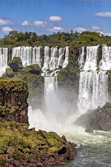 Impressive waterfalls cascade powerfully over rocks, surrounded by green vegetation and under a