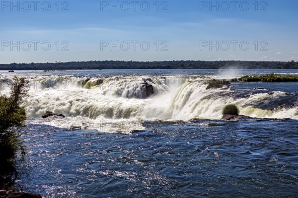 Calm river flows over rapids in bright sunlight, The waterfalls of the Iguazu between Argentina and