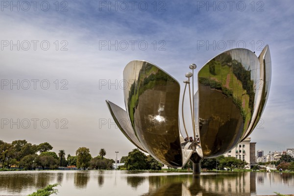 Large metal flower sculpture on the edge of a lake with a cloudy sky in the background, The lotus
