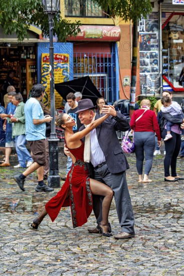 A couple performs impressive tango poses on a rain-soaked street with spectators, The colourful