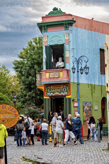 A lively place with colourful buildings and people, a statue stands on the balcony, The colourful