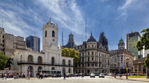 An architectural ensemble with historic buildings and a striking clock tower under a blue sky, The