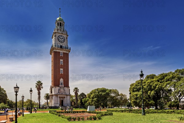 A clock tower surrounded by manicured gardens, palm trees and lanterns in a sunny park, The city of