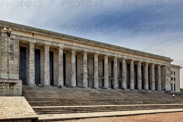 A wide building with many columns and large stairs in front of a slightly cloudy sky, The city of