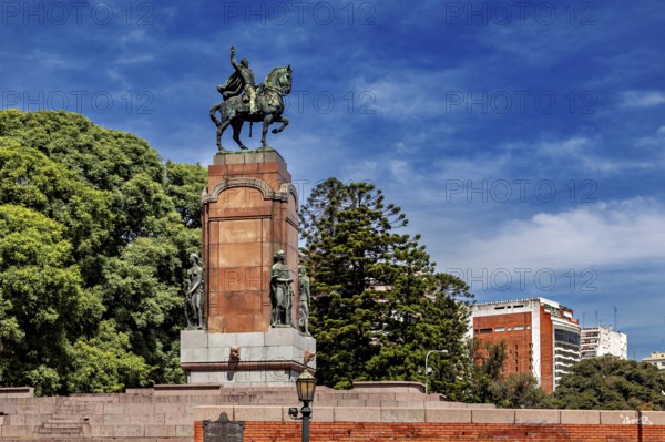 An equestrian monument on a pedestal surrounded by trees and buildings under a blue sky, The city