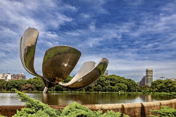 Imposing metallic flower with urban background, surrounded by a pond and trees, The lotus flower in
