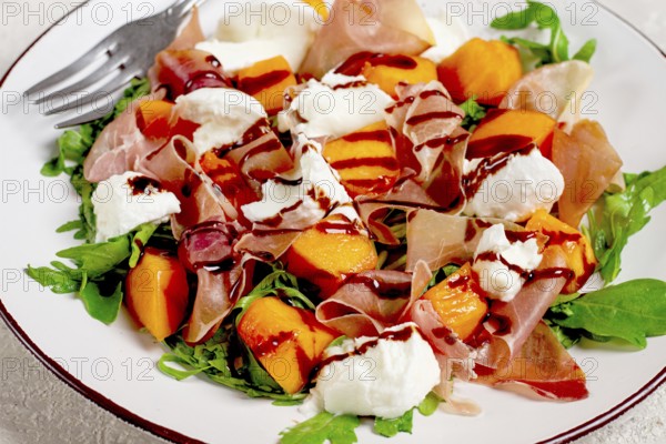 Salad with slices of ripe melon, prosciutto, mozzarella and fresh arugula, decorated with balsamic