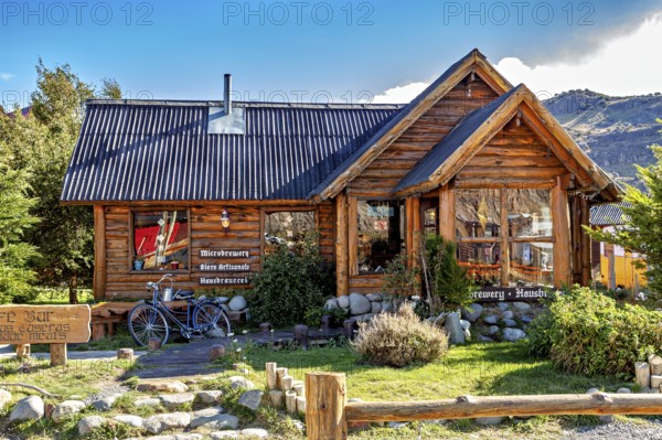 Cosy wooden house with a small garden, mountains behind it in the sunny daylight, the village of El