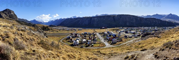 Panoramic view of a village in the valley, surrounded by high mountains and dry grassland under a