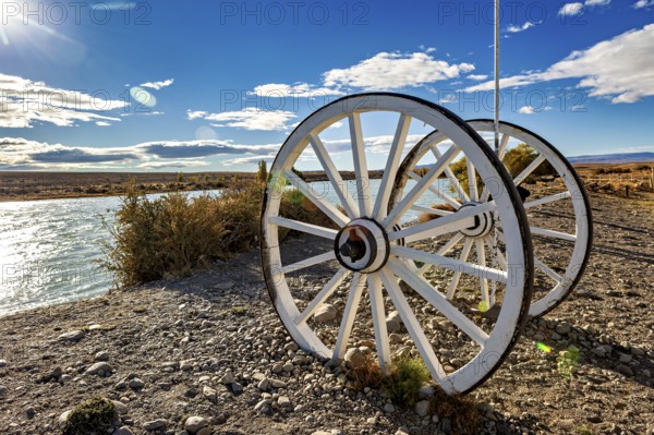 White wagon wheels on the riverbank under a blue sky with clouds, Historic horse-drawn wagon or