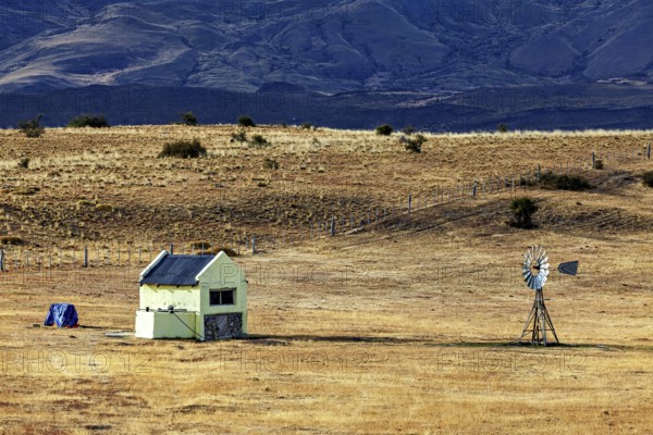 Abandoned small building with windmill in a dry, expansive landscape, The Patagonian landscape near