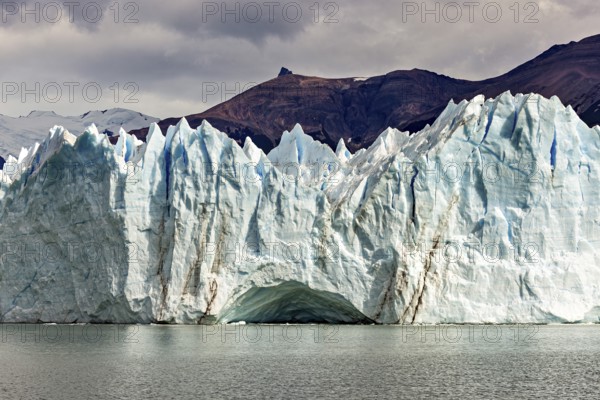Impressive ice wall of a glacier under a cloudy sky near a mountain, The glacier of Perito Moreno