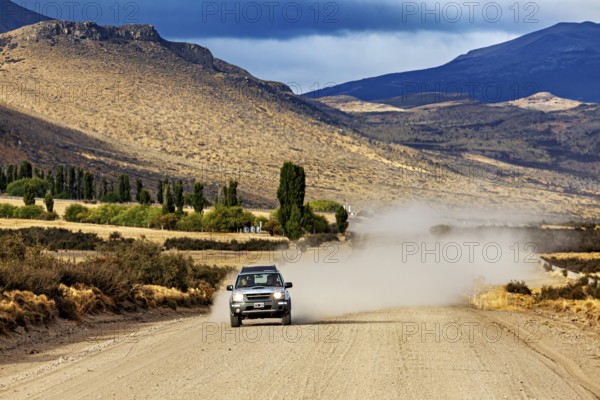 A car drives on a dusty gravel road through a mountainous landscape, Over gravel tracks through