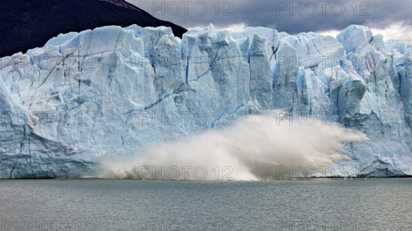 A glacier collapses into the water, blocks of ice tumble down. Threatening clouds add to the