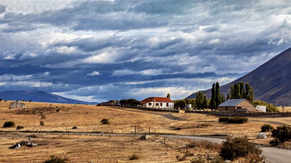 Lonely house in a rural setting with fields and mountains under a dramatic sky, The Patagonian