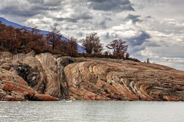Rough rocks with autumn trees under a cloudy sky by the water, The landscape at Perito Moreno in