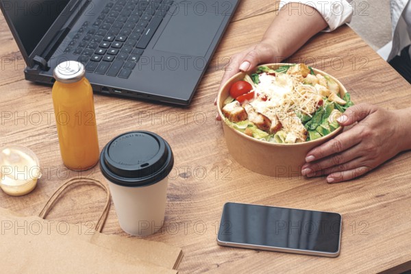A woman is working on a laptop at home, there is food on the table, salad, coffee and juice,