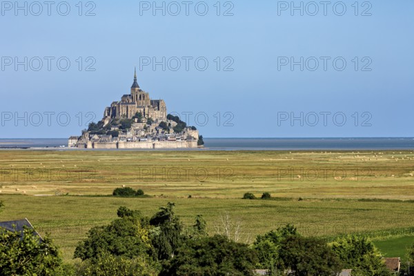 Historic abbey on a rocky island off the coast of France, surrounded by green fields and blue
