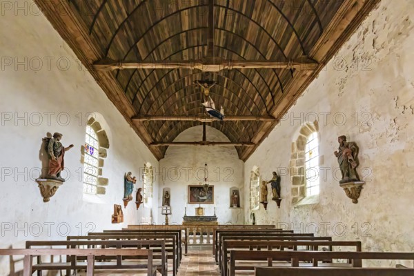 Interior view of a chapel with wooden ceiling, benches and statues on the walls, Pirou Castle in