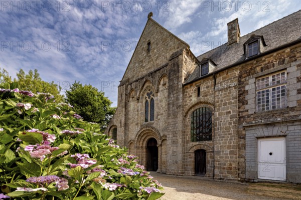 Historic stone church with colourful flowers in the foreground under a blue sky, The Abbey de La