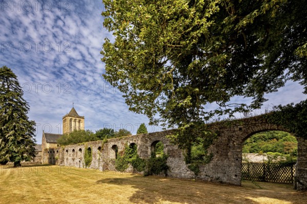 A vast stone wall next to a church, surrounded by trees under a clear sky, The Abbey of La Lucerne