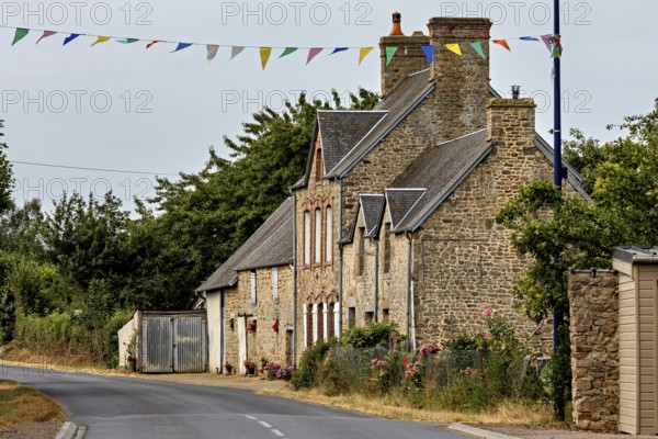 A traditional stone house on a rural road with festive garlands, Historic houses in Normandy,