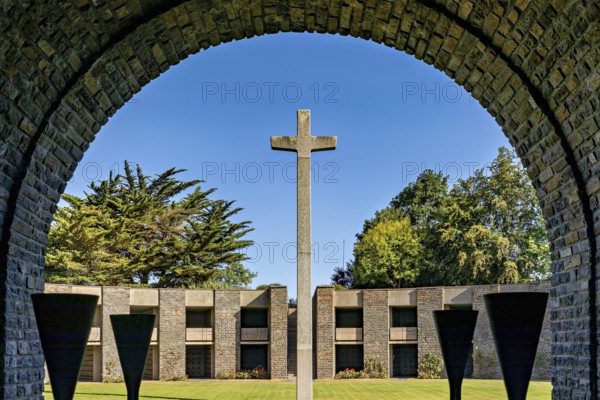 A stone cross stands in the centre of an arched passageway with a view of modern concrete