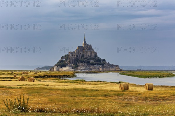 A castle island with ecclesiastical architecture in a rural landscape under a cloudy sky, Mont