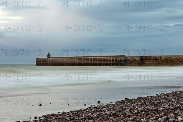A breakwater juts into the sea, surrounded by a pebble beach and a cloudy sky, The pier and beach