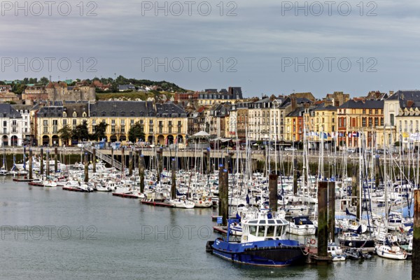 Cityscape with harbour and boats in front of a hilly backdrop under a cloudy sky, The harbour of