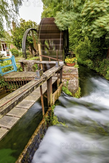 Old waterwheel next to a rushing river, surrounded by lush greenery and wooden bridges, the