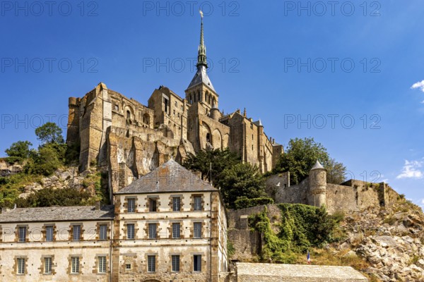 Imposing castle and fortress rising against a blue sky, with massive stone walls and towers, Mont