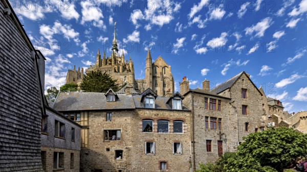 Historic stone architecture with a view of a castle under a blue sky with decorative clouds, Mont