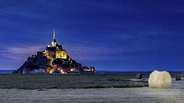 Mont Saint-Michel at night with a bale of hay in a field in the foreground, Mont Saint Michel in