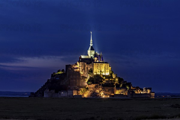 Historic monastery illuminated at night against a dark blue sky, Mont Saint Michel in Normandy,