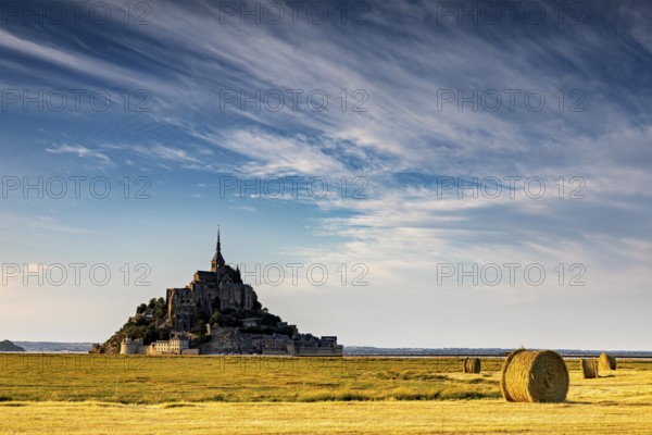 Mont Saint-Michel with dramatic sky and bales of straw in a wide field, Mont Saint Michel in